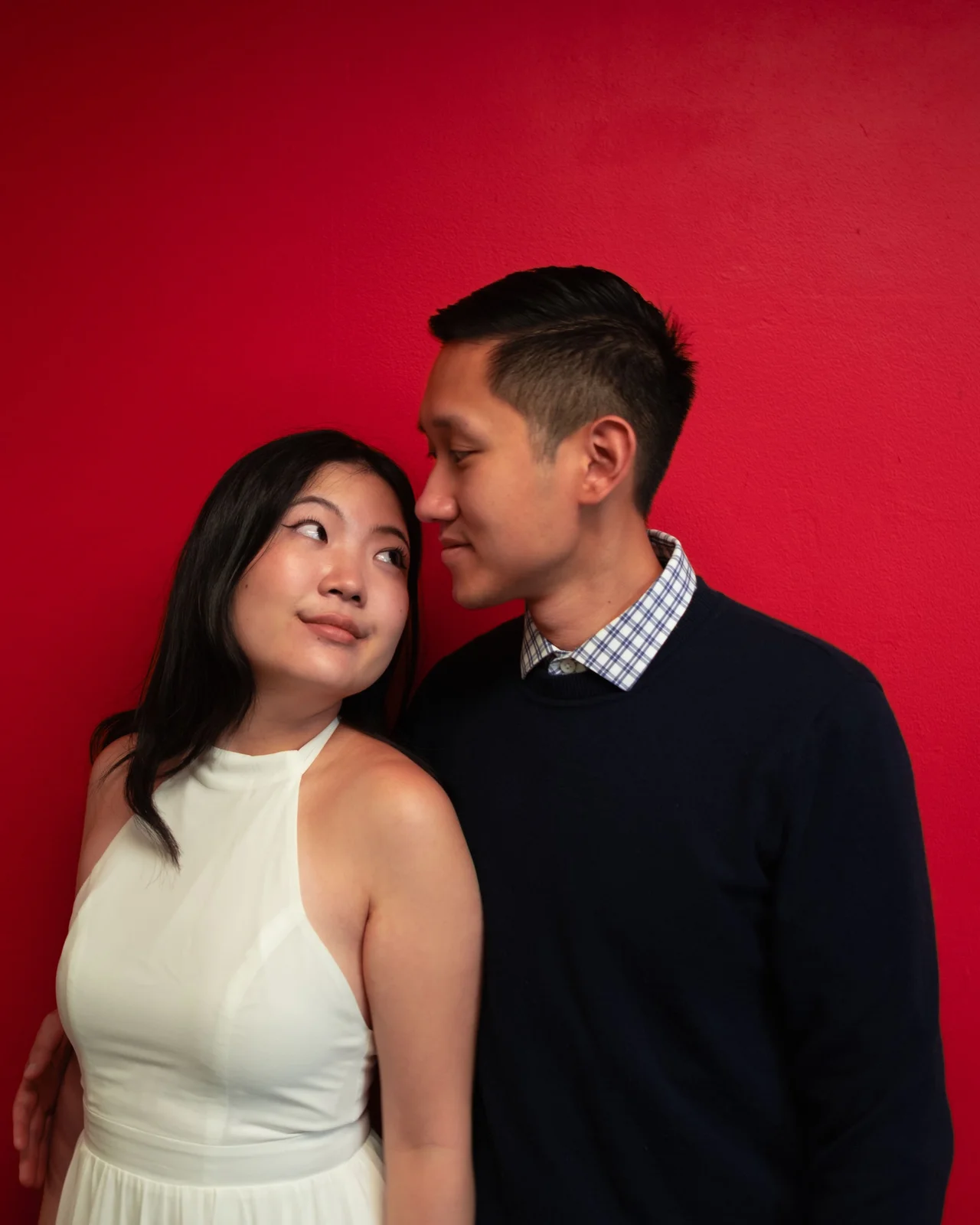 Couple looking at each other against a red wall.