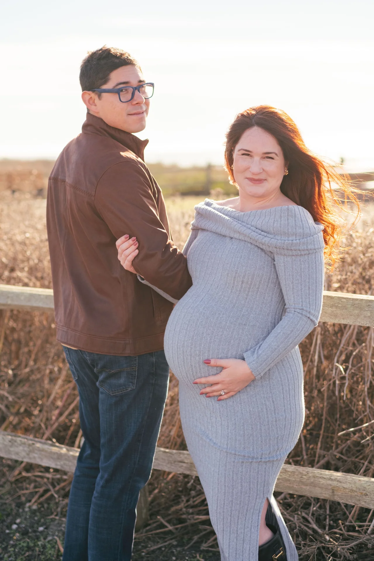 Couple beside a wooden fence, with the woman holding her pregnant belly.