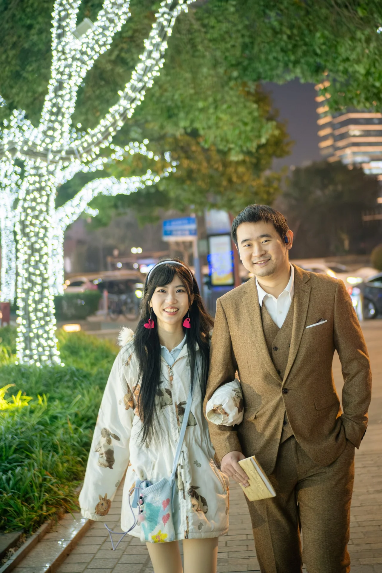 Couple standing arm in arm beside a tree covered in white lights.