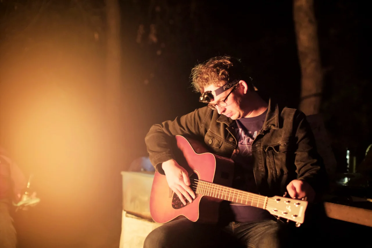 Man playing an acoustic guitar in warm light at night.