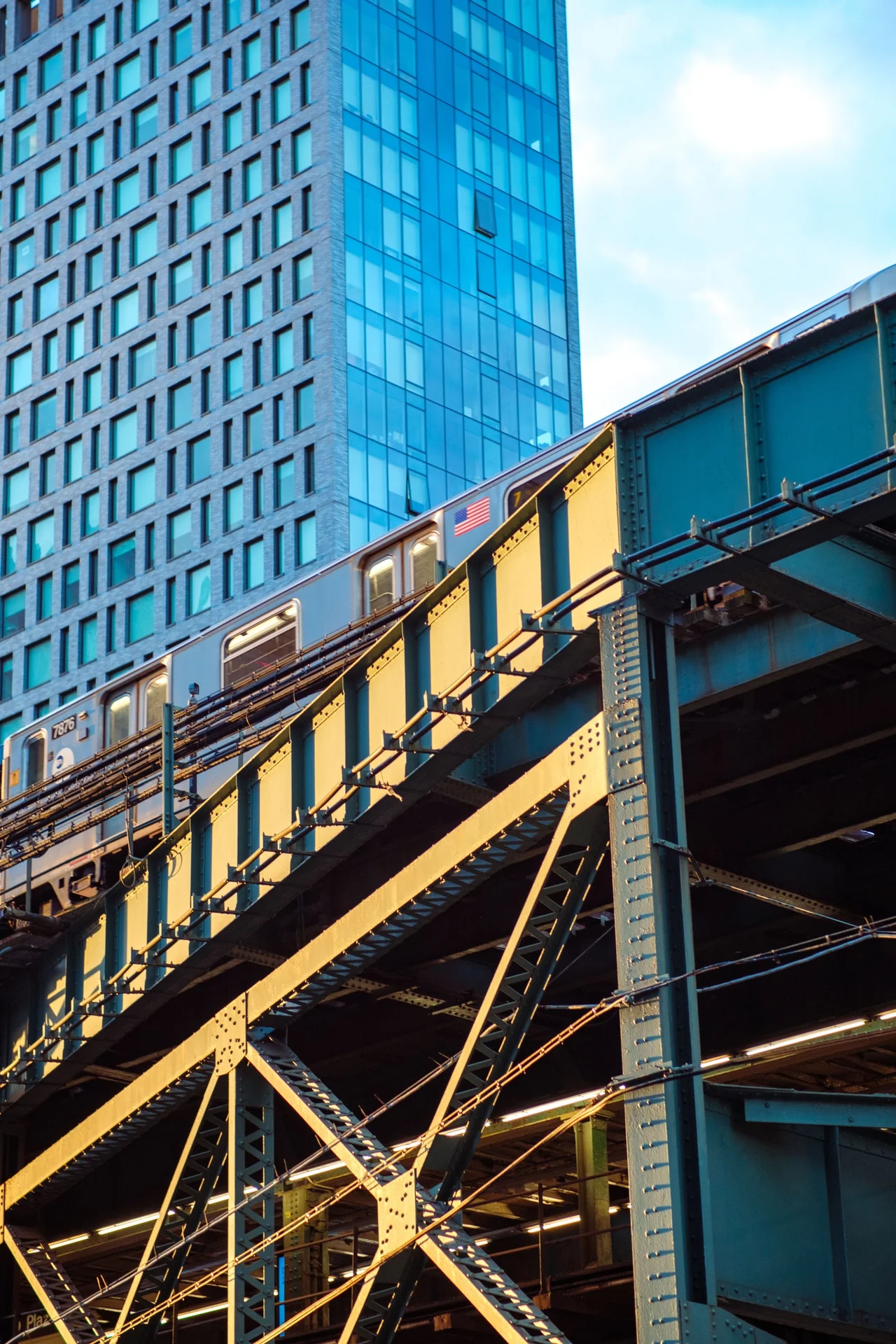An elevated train crossing a steel structure in front of a blue glass building.